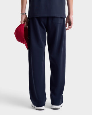 Person wearing navy blue pants holding a red cap on a white background