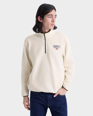 Person wearing a beige pullover with a logo on a white background