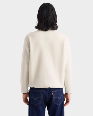 Person wearing a beige sweater and blue jeans on a white background