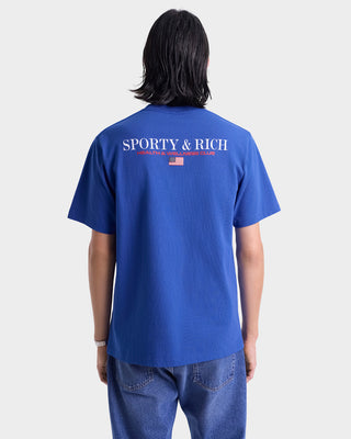 Person wearing a blue t-shirt with 'Sporty & Rich' logo on the back against a white background