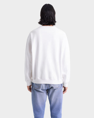 Person wearing a white sweatshirt and light blue jeans on a plain background