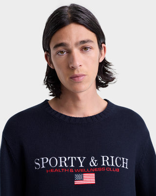 Person wearing a navy blue sweater with 'Sporty & Rich' branding on a light gray background