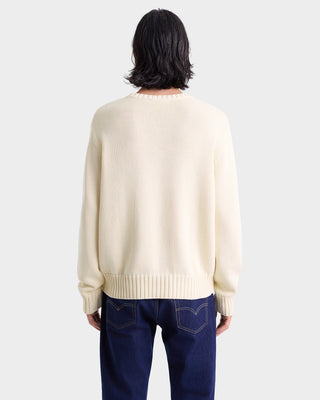 Person wearing a cream sweater and blue jeans on a white background
