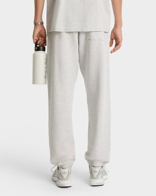 Person shown from the back wearing Syracuse Embroidered Sweatpant in heather gray/navy and sneakers, holding a white water bottle. Sweatpants are made with USA-grown cotton.
