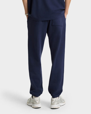 Person wearing the Syracuse Embroidered Sweatpant in Navy/White, made from USA-grown cotton, paired with white sneakers, standing with hands in pockets and facing away.