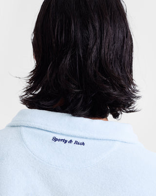 Person with medium-length dark hair, wearing the Eden Script Terry Polo in Ciel/Navy, featuring Sporty & Rich embroidery on the back collar. Made from cotton in Portugal.