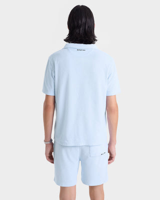 Person with shoulder-length dark hair wears the Eden Script Terry Polo - Ciel/Navy, made in Portugal, with matching shorts, shown from the back.