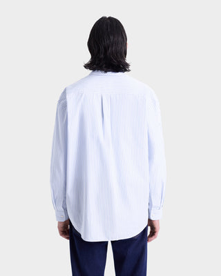 A person with shoulder-length dark hair is seen from behind wearing the Eden Script Oversized Shirt in blue/white stripe and dark pants.