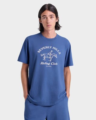 Person wearing a blue t-shirt with 'Beverly Hills Riding Club' text and graphic on a light gray background