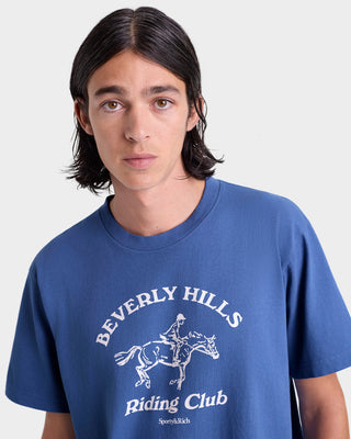 Person wearing a blue t-shirt with 'Beverly Hills Riding Club' print on a white background