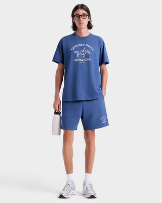 Person wearing a blue t-shirt and shorts with a logo, holding a white bag on a white background