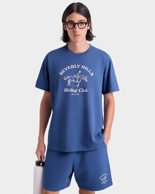 Person wearing a blue 'Beverly Hills Riding Club' t-shirt and shorts on a white background