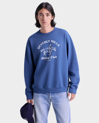 Person wearing a blue sweatshirt with 'Beverly Hills Riding Club' text and graphic on a white background