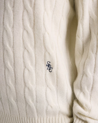 Close-up of a cable-knit sweater with a logo on a white background