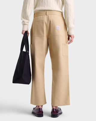 Person wearing beige pants holding a black bag on a white background