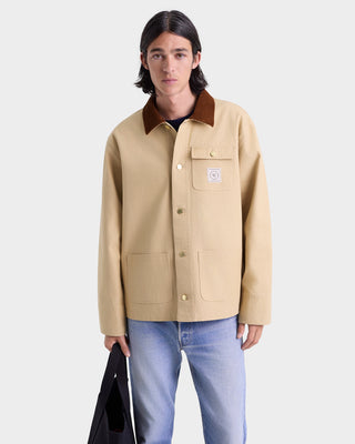 Person wearing a beige jacket with brown collar on a white background