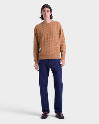 Man wearing a brown cable knit sweater and blue pants on a white background
