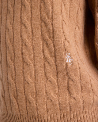 Close-up of a brown cable-knit sweater with a brand logo.