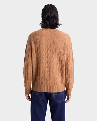 Person wearing a brown cable knit sweater and blue jeans on a white background