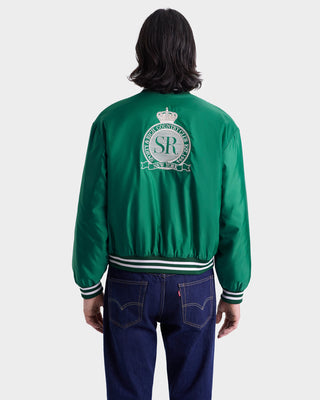 Person wearing the Royal Club Nylon Varsity Jacket in Spring Green/White with an embroidered crest and blue jeans, shown from the back.