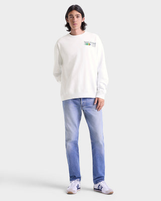 Person wearing a white sweatshirt with a logo and light blue jeans on a white background