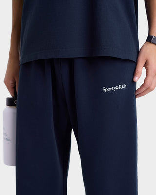 Navy blue pants with 'Sporty&Rich' logo worn by a person, holding a water bottle.