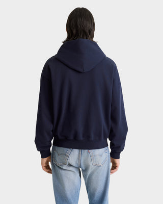 Person wearing a navy blue hoodie and light blue jeans on a white background