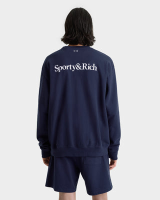 Person wearing a navy blue 'Sporty&Rich' sweatshirt and shorts on a white background