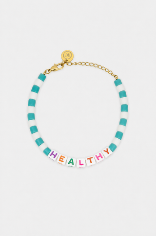 The Healthy Pearl/Bead Bracelet features gold pearls, colored beads, and white letter beads spelling HEALTHY on a gray background. It has an adjustable design for a comfortable, perfect fit.