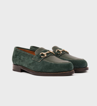The Penny Loafer - Pine is a green suede loafer, handmade in Spain from full grain leather, featuring a gold metal bit detail and brown soles, displayed on a plain white background.
