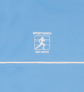 The Runner Track Jacket - Atlantic/White is a blue, high-quality fabric jacket featuring a printed running person logo with SPORTY & RICH STAY ACTIVE text above and below.