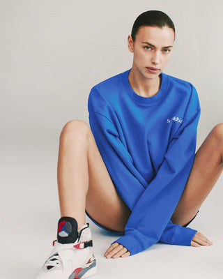 Model wearing royal blue crewneck sweatshirt with white 'Sporty & Rich' text on the left chest, featuring ribbed hem and cuffs.