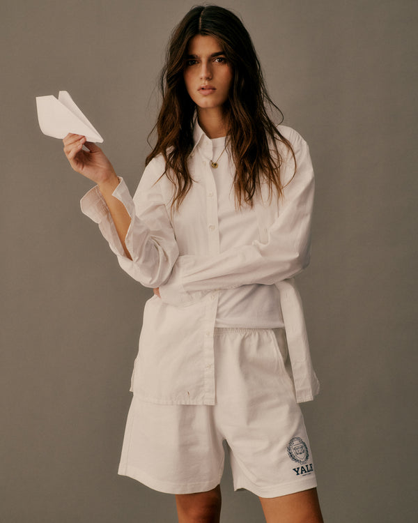 Woman in a white outfit holding a paper airplane against a gray background