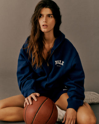 Woman wearing a Yale hoodie holding a basketball against a gray background