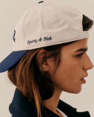 Person wearing a cap with 'Sporty & Rich' branding on a plain background