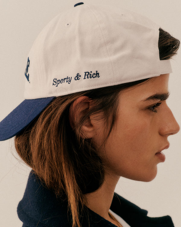 Person wearing a cap with 'Sporty & Rich' branding on a plain background