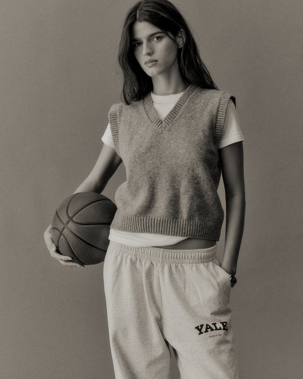 Person wearing a sleeveless sweater and pants holding a basketball against a plain background