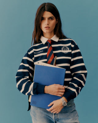 Person wearing a striped shirt with a tie, holding a blue folder against a blue background