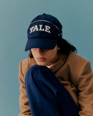 Person wearing a navy 'YALE' cap against a blue background