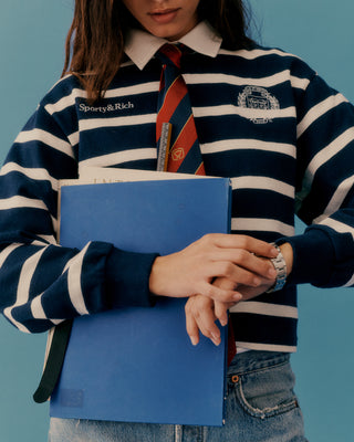 Person wearing a striped shirt with a visible brand logo, holding a blue folder against a blue background.