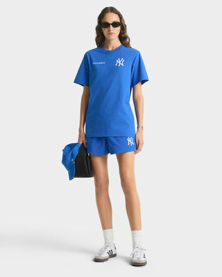 Person wearing a blue outfit with a logo, holding a blue bag on a white background