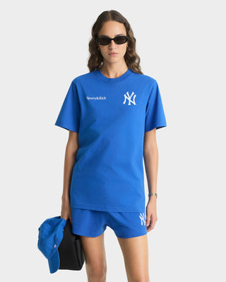 Person wearing a blue t-shirt and shorts with logos, holding a blue bag on a white background