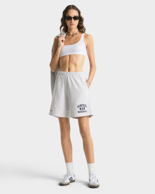 Woman wearing a white tank top and skirt with sunglasses on a plain background
