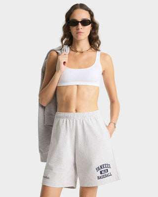 Woman wearing a white sports bra and gray shorts with 'Yankees' branding on a light gray background