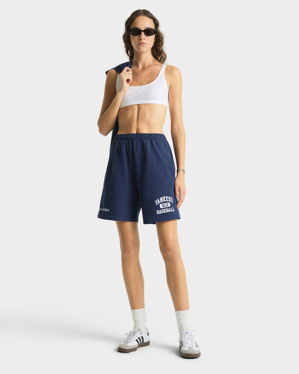 Woman wearing navy shorts with text, white sports bra, and sneakers on a white background
