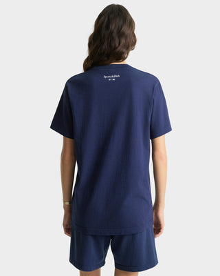 Person wearing a navy blue t-shirt with a brand logo on the back, standing against a white background