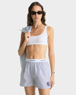 Woman wearing a white sports bra and striped shorts with a visible brand logo on a plain background