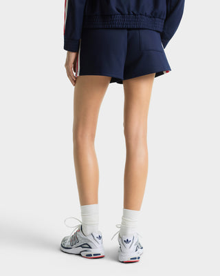 Person wearing navy tracksuit, white socks, and Adidas sneakers on a white background