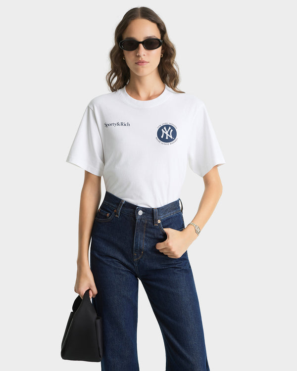 Person wearing a white t-shirt with a logo and dark jeans on a white background