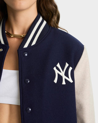 Navy blue varsity jacket with white lettering worn by a person, on a plain background